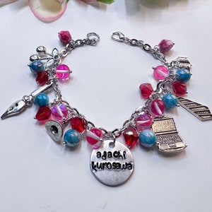 Op de afbeelding: Een zilveren armband met roze, rode en blauwe kralen. De bedels omvatten een laptop, een stropdas, een hoed, een pen en een label met de tekst "agachi kurosawa".