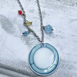 May include: A silver chain necklace with a blue and white circle pendant. The pendant has a light blue border and a white center. The necklace also has several small blue, yellow, and red beads.