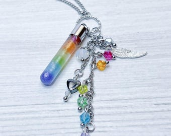 Könnte beinhalten: Eine Halskette mit einem Regenbogen-Glasröhren-Anhänger, einer silbernen Kette, einem Herz-Anhänger und Kristallperlen. Die Halskette hat auch einen silbernen Engelsflügel-Anhänger.
