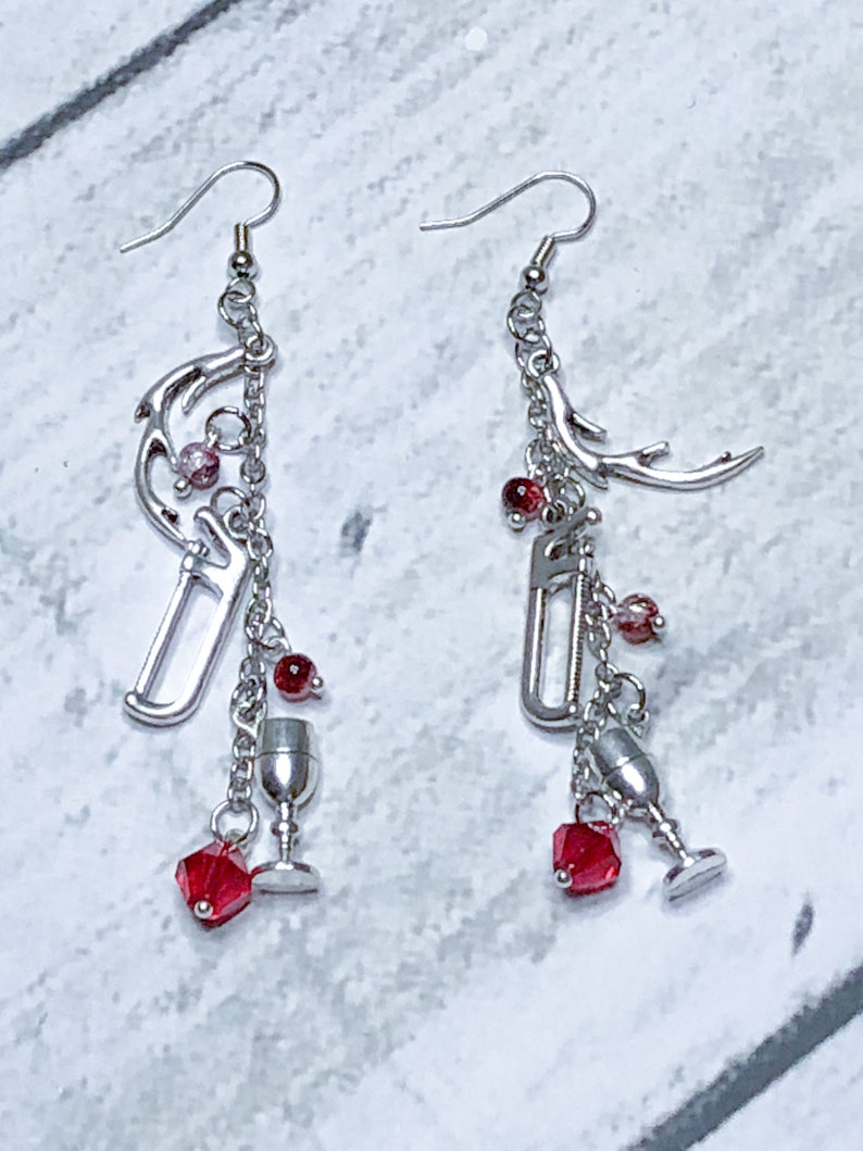 May include: A pair of silver dangle earrings with red crystal beads, a silver goblet charm, and a silver antler charm.