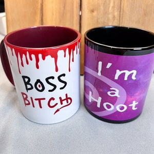 Puede incluir: Dos tazas de cerámica. Una taza blanca con pintura roja goteando y las palabras "BOSS BITCH" en negro y rojo. La otra taza es morada con las palabras "I'm a Hoot" en blanco.