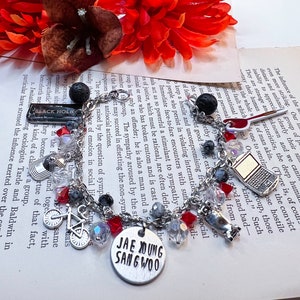 May include: A silver charm bracelet featuring black lava beads, red and clear glass beads, and a variety of charms, including a bicycle, a skateboard, a laptop, a book, and a charm with the text "JAE YOUNG SANG WOO".