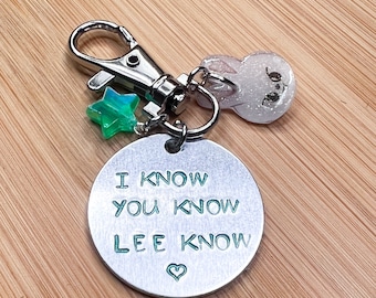 May include: A silver keychain with a round metal tag that says "I know you know Lee know" with a heart symbol. The keychain also has a green star charm and a white bunny charm.