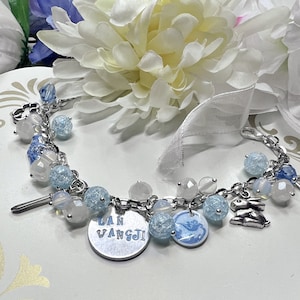 May include: A silver charm bracelet with blue and white beads, charms, and a charm with the text "LAN WANGJI".