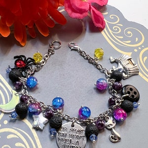 May include: A silver charm bracelet with a variety of charms, including a spider, a crescent moon, a star, a button, a cat, and a charm that says "So sharp you won't feel a thing". The bracelet also features black lava beads, purple and blue glass beads, and clear glass beads.