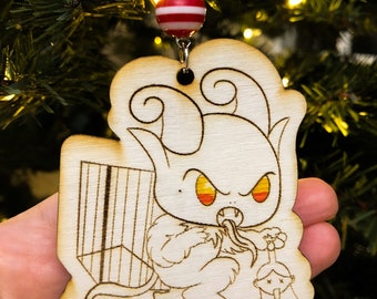 Könnte beinhalten: Ein Weihnachtsbaumschmuck aus Holz mit einem Cartoon-Teufel, der ein Geschenk und eine Glocke hält. Der Schmuck ist in Braun- und Weißtönen bemalt.