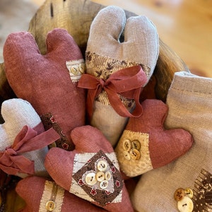 May include: A collection of handmade fabric hearts in shades of brown and beige. The hearts are decorated with buttons and fabric scraps.