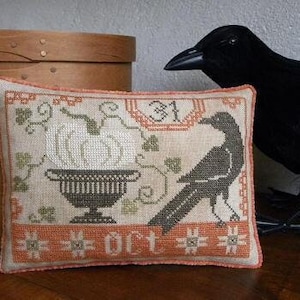 May include: A white and orange embroidered pillow with a black crow, a pumpkin in a pot, and the text "31 Oct".