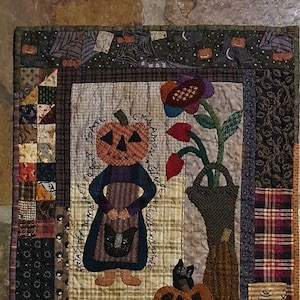 May include: A quilted wall hanging with a patchwork design featuring a pumpkin with a face, a black cat, and the text "Make Space for the Weird & Wonderful." The bottom right corner has the text "Pumpkin Spice."