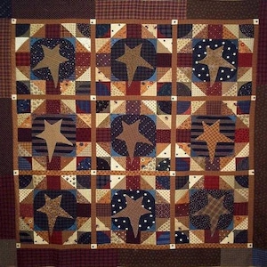 May include: A quilt with a patchwork design featuring a repeating pattern of brown stars on a navy blue background. The quilt is made up of various fabrics in shades of brown, red, and blue.