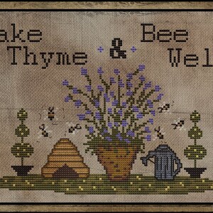 May include: Cross-stitch artwork in a wooden frame, with the text "Take Thyme & Bee Well." The design includes a pot of purple flowers, a beehive, bees, and topiary trees. A watering can is also present, all on a green base.