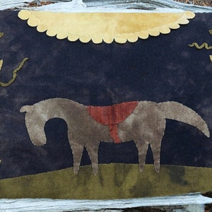 May include: A dark blue textile with a horse, flowers, and a sun design. The horse is brown with a red saddle. Flowers with pink and green petals are on either side of the horse. A yellow sun shape is at the top.
