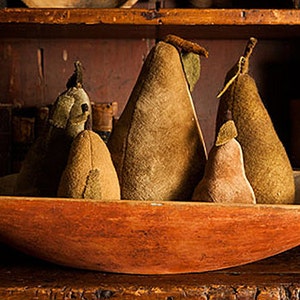 May include: Four brown fabric pears in a wooden bowl. The pears are arranged in a row, with the largest pear in the center. The bowl is a rustic, reddish-brown color.