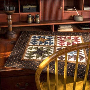 Peut inclure: Une courtepointe marron et noire avec un motif géométrique. La courtepointe est composée de quatre carrés, chacun avec un motif différent. La courtepointe est sur une table en bois avec une chaise au premier plan.