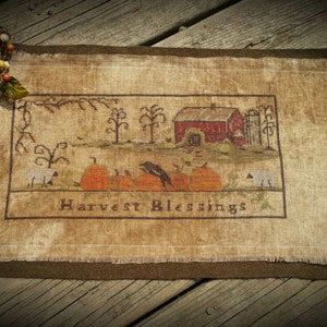 Può includere: Arazzo rettangolare rustico con una scena del raccolto autunnale. Il disegno presenta un fienile rosso, zucche e la scritta "Harvest Blessings". Una candela in un barattolo di vetro con una ghirlanda decorativa si trova in alto a sinistra.