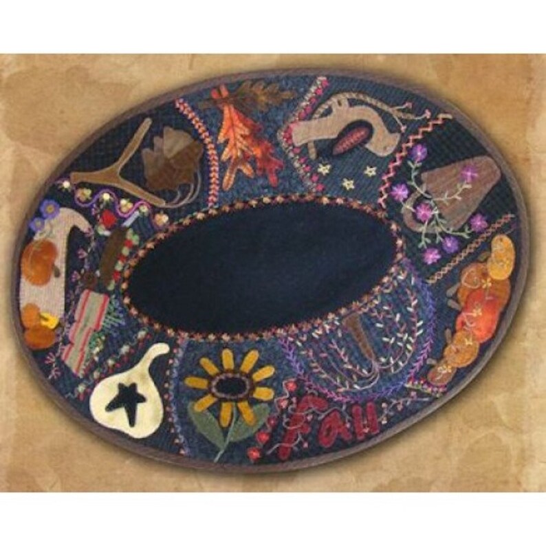 May include: An oval-shaped, denim-colored decorative piece with a dark center. The border is adorned with embroidered fall-themed elements like leaves, sunflowers, and the word "FALL". The design incorporates various colors and textures, creating a rustic aesthetic.