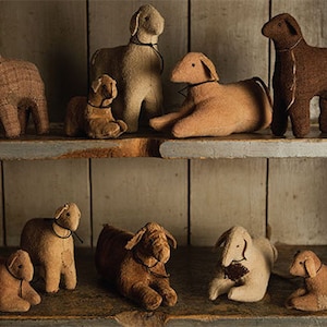 May include: A collection of handcrafted sheep figurines in various sizes and shades of brown and beige. Some sheep are standing, while others are lying down. Each has a simple black cord around its neck, displayed on rustic wooden shelves.
