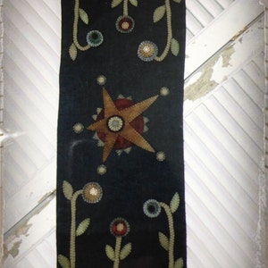May include: A dark blue felt runner with a star and flower design. The runner has a scalloped edge with a row of circles in various colors.