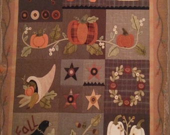 Könnte beinhalten: Ein Patchwork-Quilt mit Herbstthema. Der Quilt zeigt verschiedene Quadrate mit Bildern von Kürbissen, Sternen, einem Haus, einem Füllhorn und einer Krähe. Das Wort "Fall" ist auf dem Quilt geschrieben.