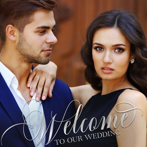 May include: A wedding sign featuring a photograph of a couple, with the text Welcome TO OUR WEDDING, Frank & Lori, and August 29, 2019. The man wears a navy blue blazer and white shirt, while the woman wears a black sleeveless dress and earrings.