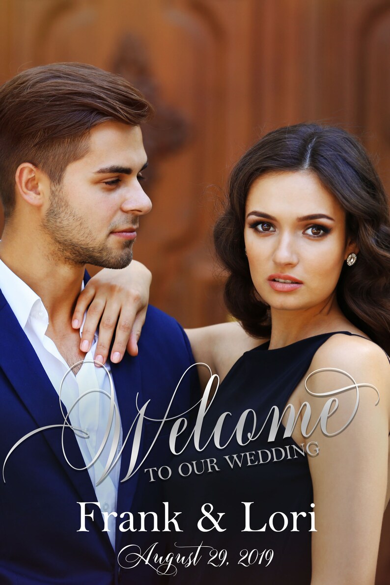 May include: A wedding sign featuring a photograph of a couple, with the text Welcome TO OUR WEDDING, Frank & Lori, and August 29, 2019. The man wears a navy blue blazer and white shirt, while the woman wears a black sleeveless dress and earrings.