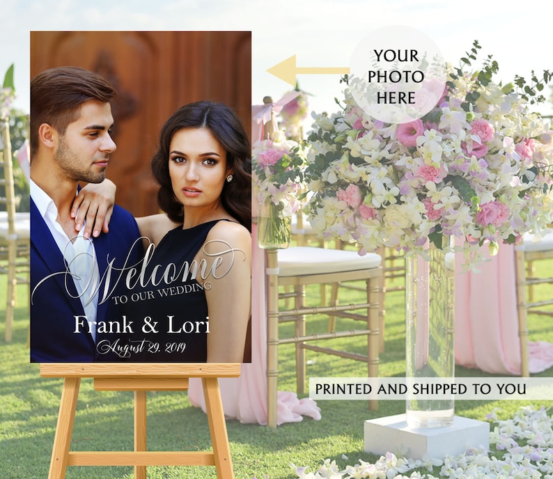 May include: A rectangular wedding welcome sign on a wooden easel featuring a photograph of a couple. The text reads Welcome to our wedding, Frank & Lori, and August 29, 2019. A circular graphic with an arrow points to the photo area with the text Your photo here.