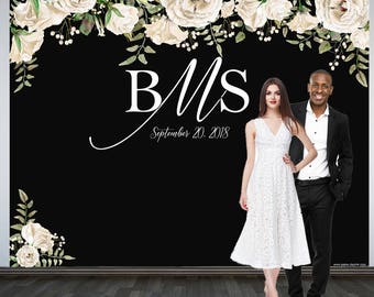 May include: A black and white wedding backdrop with white flowers and greenery. The text "B&M" and "September 20, 2018" is written in white on the backdrop. A couple is standing in front of the backdrop.