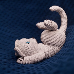 May include: A crocheted grey cat toy with blue eyes, lying on a blue textured surface.