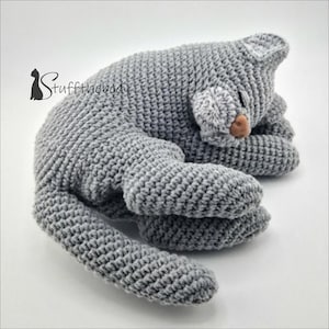 May include: A gray crocheted cat toy in a sleeping position. The cat has a white patch on its face and a brown nose.