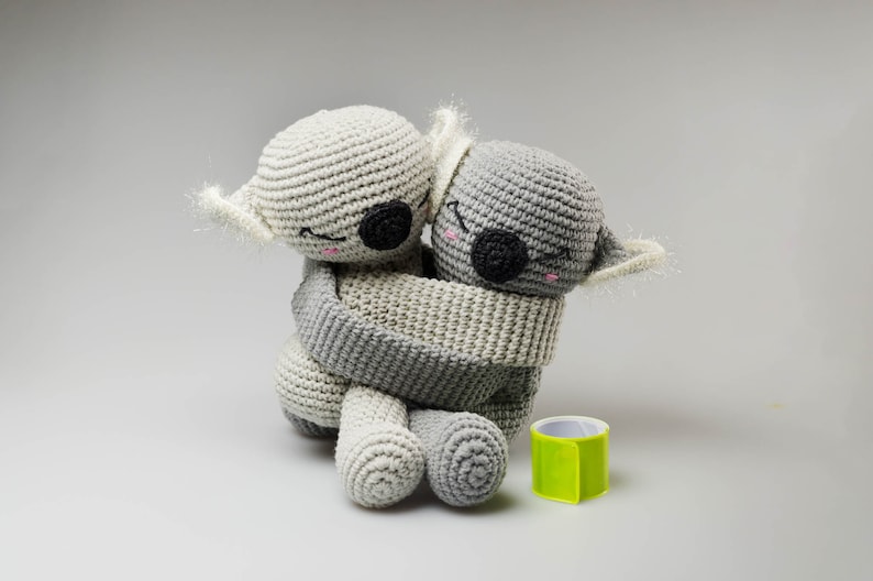 May include: Two gray crocheted koala plushies hugging each other. The koala on the left is white and the koala on the right is gray.