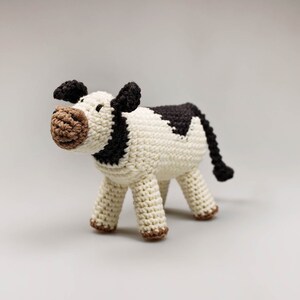 May include: A crocheted stuffed cow toy with black and white markings. The cow has a brown nose and black ears.