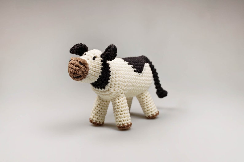 May include: A crocheted stuffed cow toy with black and white markings. The cow has a brown nose and black ears.