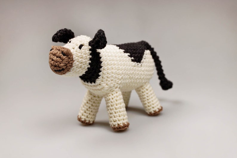 Cute crochet cow amigurumi with black spots, brown muzzle, and a small tail, handmade stuffed farm animal toy