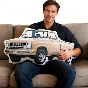 May include: A die-cut scatter cushion shaped like a vintage beige pickup truck. The cushion features a detailed graphic print of the truck's front grille, headlights, side profile, and wheels, capturing the classic design of a light-duty truck.