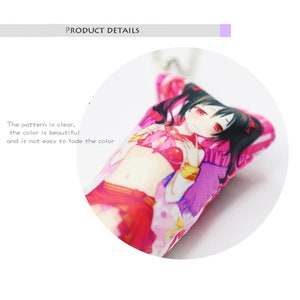May include: A pink and white plush pillow with a colorful anime character printed on it. The character has long black hair, red eyes, and is wearing a pink and white outfit.