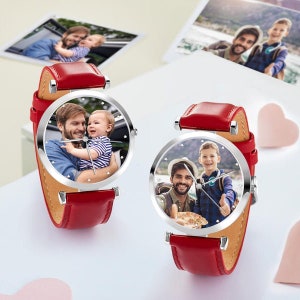 May include: Two personalized watches with red leather straps and silver-tone cases. Each watch face displays a family photo. The watches are on a white surface, with additional photos in the background.