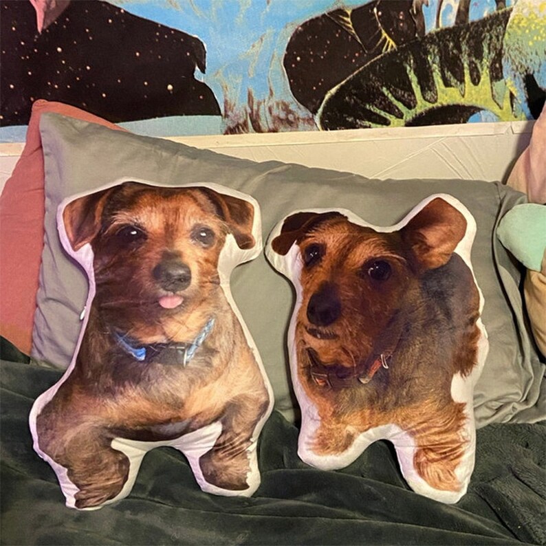 May include: Two brown and white dog-shaped pillows with a white background. The pillows are on a gray and brown surface.