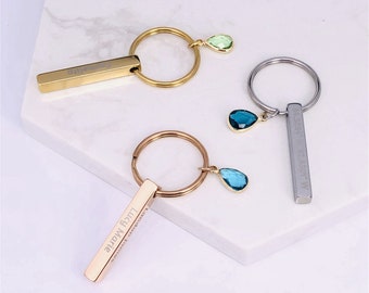 May include: Three gold, silver, and rose gold keychains with personalized bars and teardrop-shaped crystal charms. The charms are green, blue, and light blue.