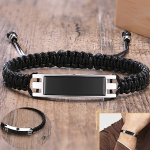 May include: Black braided bracelet with a silver rectangular plate. The plate has a black surface and can be engraved.