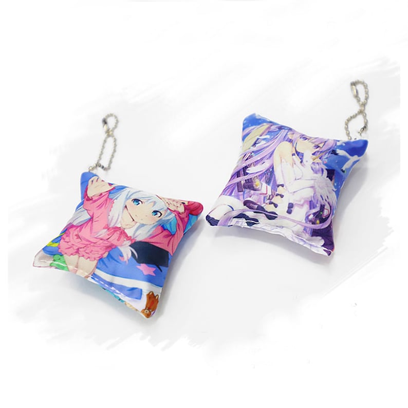 May include: Two small, square-shaped pillows with anime character designs. The pillows are attached to silver keychains. The pillow on the left features a girl with long, blue hair wearing a pink and blue outfit. The pillow on the right features a girl with long, purple hair wearing a white and purple outfit.