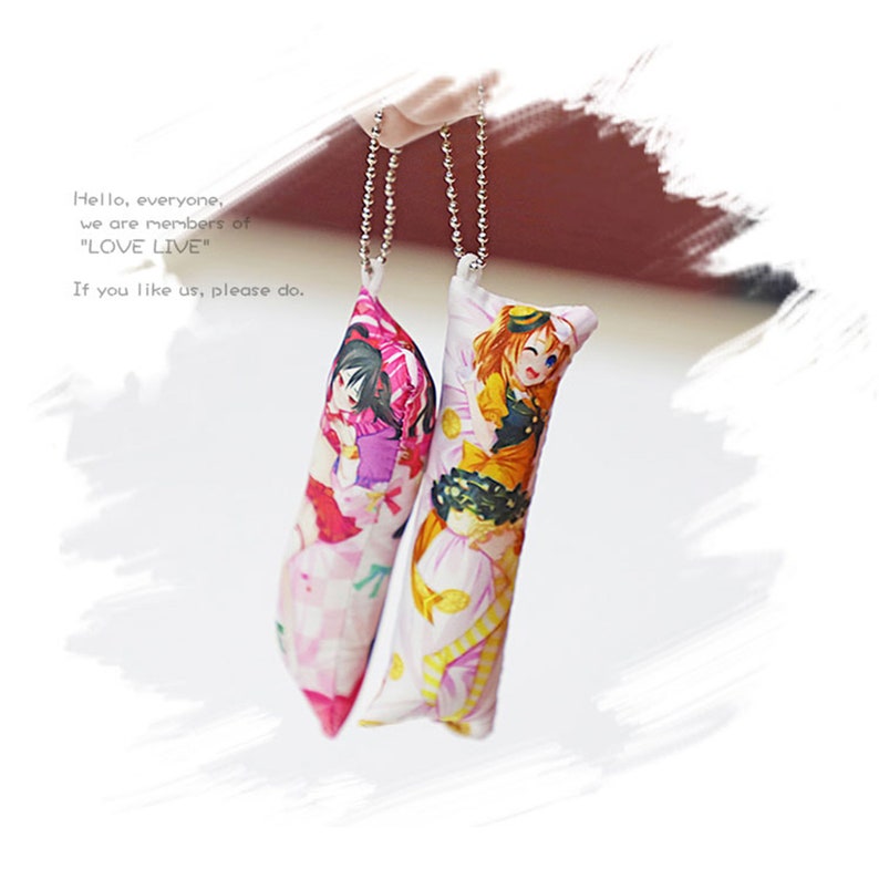 May include: Two colorful keychains featuring anime characters from the "Love Live!" franchise. The keychains are shaped like pillows and have a chain attached to the top.