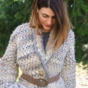 Peut inclure: Un long cardigan en crochet de couleur gris clair et beige avec une ceinture marron. Le cardigan a un col châle et une fermeture boutonnée.