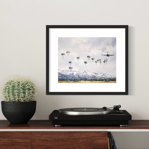 May include: A watercolor painting of a military plane dropping paratroopers over a mountain range. The plane is flying towards the viewer, and the paratroopers are descending in a line. The sky is cloudy, and the mountains are snow-capped.