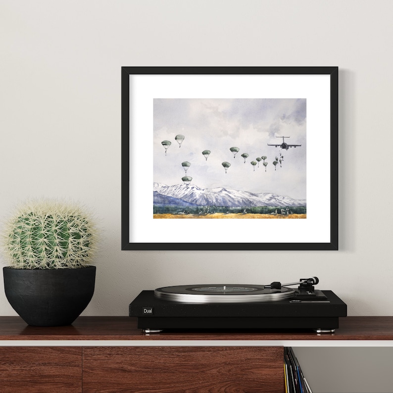 May include: A watercolor painting of a military plane dropping paratroopers over a mountain range. The plane is flying towards the viewer, and the paratroopers are descending in a line. The sky is cloudy, and the mountains are snow-capped.