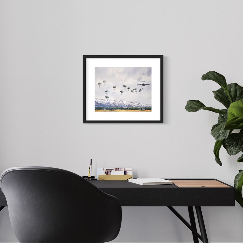 May include: A framed watercolor painting of a military plane dropping paratroopers over a snowy mountain range. The plane is flying high in the sky, and the paratroopers are descending with their parachutes open.