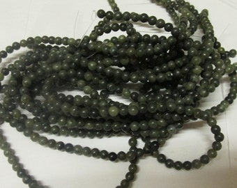 Può includere: Un filo di perline rotonde verde scuro, probabilmente in pietra, per la creazione di gioielli.