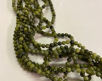 Può includere: Un filo di perle di giada verde, ogni perla è rotonda e liscia. Le perle sono infilate su un filo trasparente e sono disposte in un mucchio sciolto.
