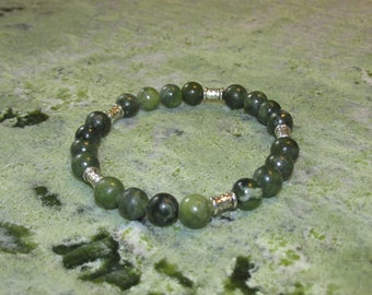 May include: A green jade stone bracelet with silver accents. The bracelet is made of round beads and is strung on a stretchy cord.