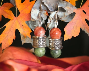May include: A pair of dangle earrings with a silver Celtic knot design, featuring a red and green stone bead combination.