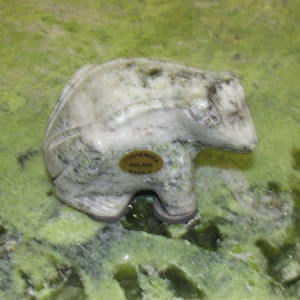 May include: A white marble sculpture of a bear, with green veins running through the marble. The sculpture is sitting on a green marble surface. The sculpture has a gold label that reads "Connemara Ireland Marble".